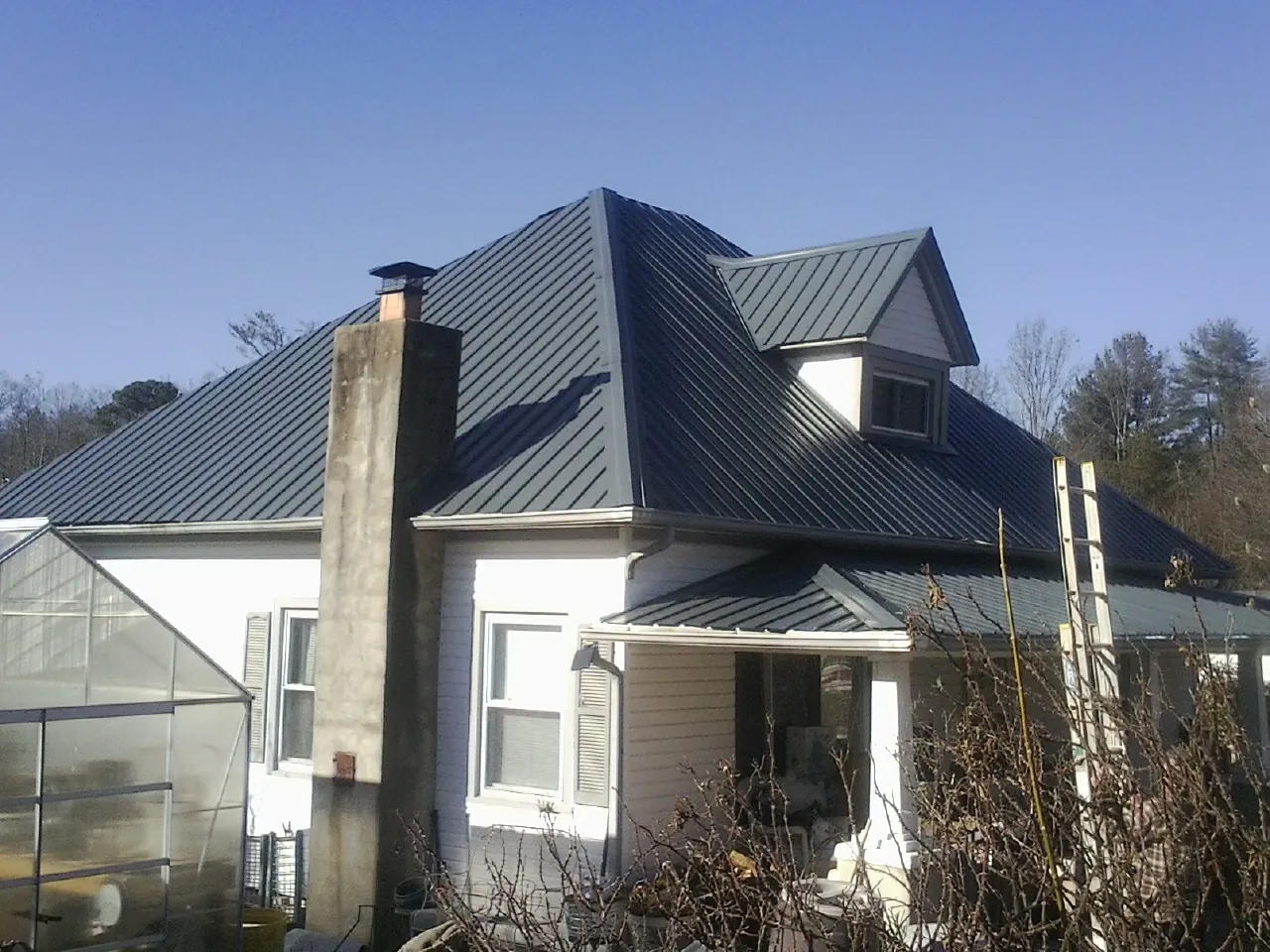 Dark blue standing seam metal roof on a white farmhouse with dormer — Slate & Tile Roof Repair by Roofing Brothers in Pennsboro
