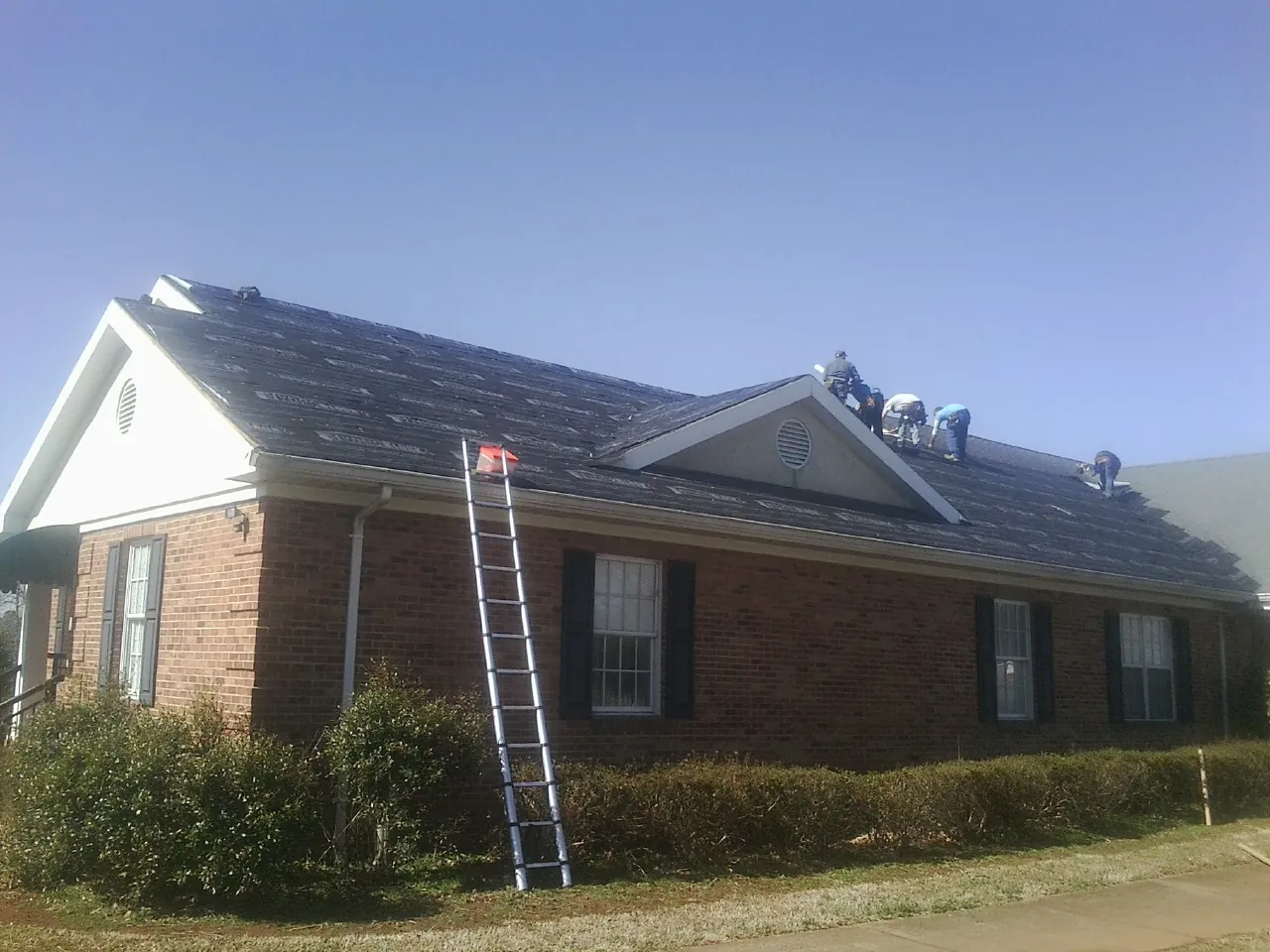 Crew tearing shingles off a brick ranch roof with a ladder set — Metal Roof Repair work by our crew in Pennsboro