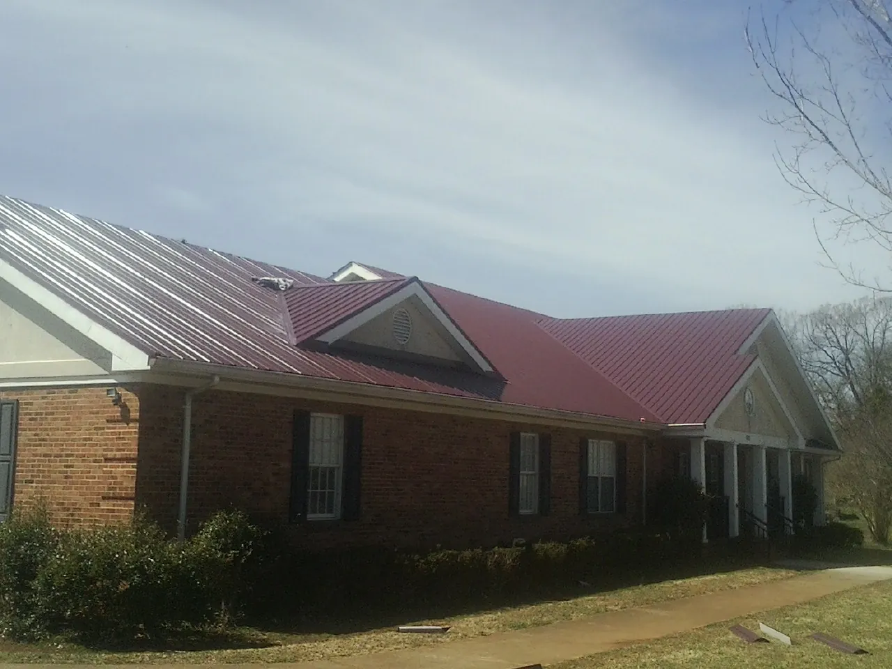 Red metal roof with gabled entries on a long brick building, from a Hail Damage Roof Repair job in Pennsboro