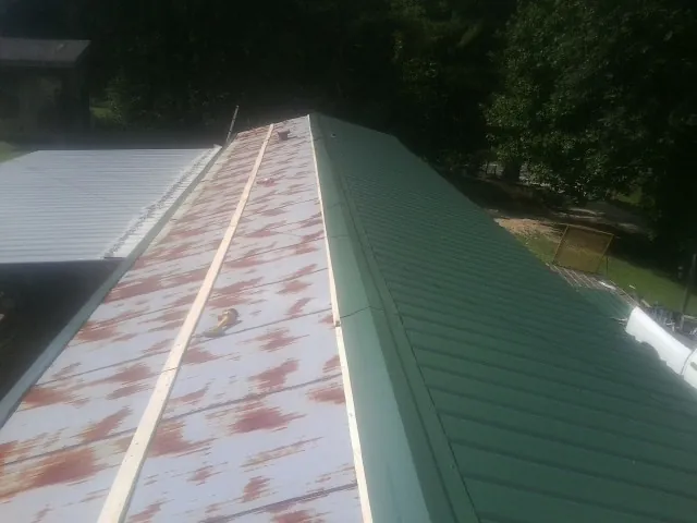 Old rusted panels beside newly installed green metal roofing — Wind Damage Roof Repair by Roofing Brothers in Pennsboro