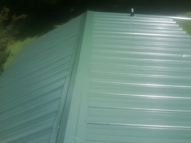 New green metal panels meeting at the ridge of a roof — Flat Roof Repair work by our crew in Pennsboro