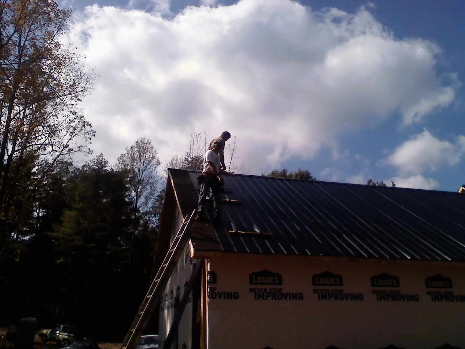 Roofer fastening dark metal panels high against a cloudy sky, from a Roof Inspection job in Pennsboro
