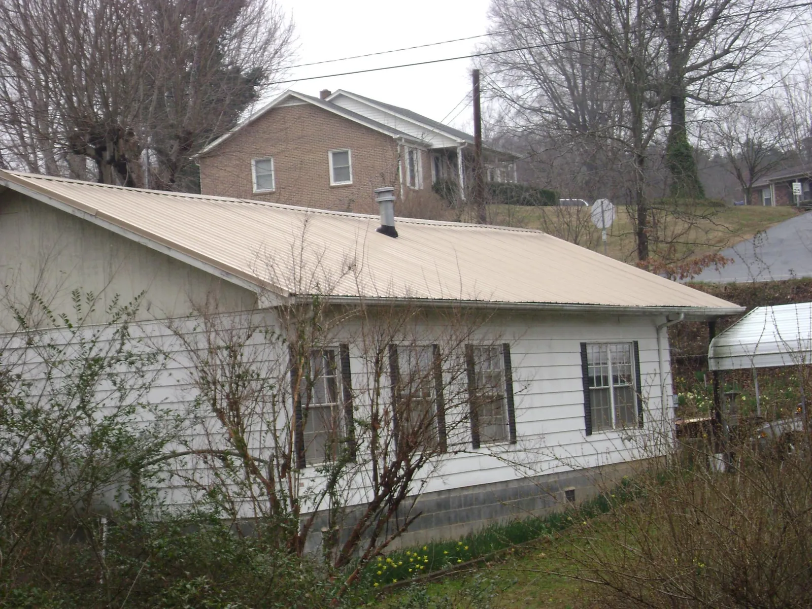 Tan metal roof on a white sided house set into a hillside — Commercial Roofing by Roofing Brothers in Pennsboro