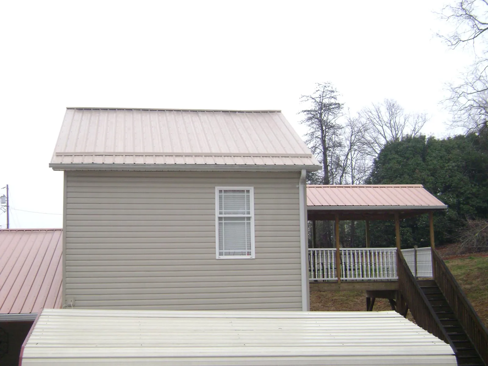 Tan metal roofs on a two story addition and attached porch, from a Roof Replacement job in Pennsboro